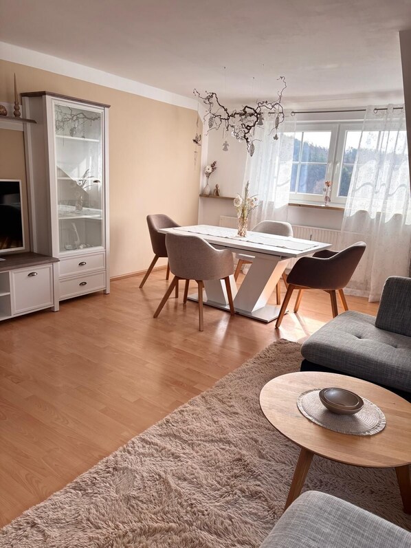 Una sala de estar moderna con comedor, un sofá, una mesa de centro y un televisor.