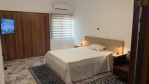 Ein Schlafzimmer mit Bett, Nachttischlampen, einem Fernseher, einem Kleiderschrank und einer Klimaanlage.
