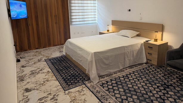 Ein Schlafzimmer mit Bett, Nachttischen, Fernseher, Kleiderschrank und einem Fenster mit Jalousien.