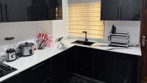 Eine moderne Küche mit schwarzen Schränken, einer Marmorarbeitsplatte, einem eingebauten Herd, einem Mixer und einer Kaffeemaschine.
