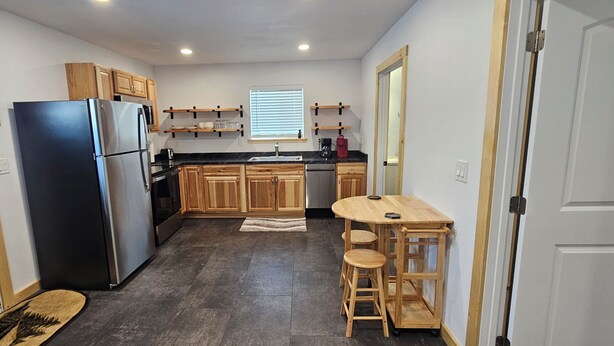 Una cocina funcional con refrigerador, estufa, gabinetes de madera, un lavamanos y una pequeña mesa de madera con taburetes.
