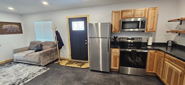 A compact kitchen with a refrigerator, microwave, oven, and wooden cabinets.