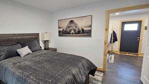 Un dormitorio con cama, lámpara de noche, perchero y puerta.