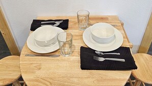 Una mesa redonda de madera con dos platos blancos, una copa y cubiertos.