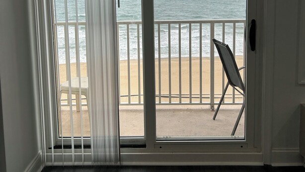 A room with a large sliding glass door leading to a balcony with a view of the ocean. - Cozy 2-bedroom condo in quaint Virginia Beach with AC and gym (Virginia Beach)