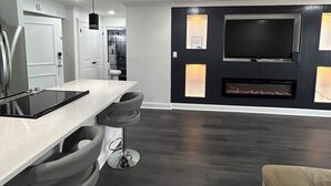 A modern kitchen with a bar area, a flat-screen TV mounted on a dark wall, and a minimalist design. - Cozy 2-bedroom condo in quaint Virginia Beach with AC and gym (Virginia Beach)
