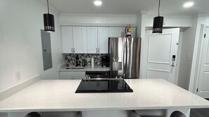 A modern kitchen with a central island, two bar stools, and pendant lighting. - Cozy 2-bedroom condo in quaint Virginia Beach with AC and gym (Virginia Beach)
