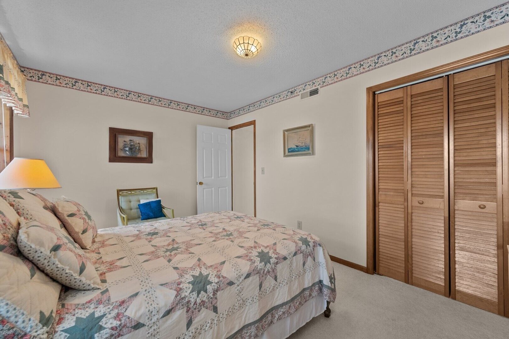 Un dormitorio con una cama, una mesita de noche, una lámpara, una puerta y un armario.