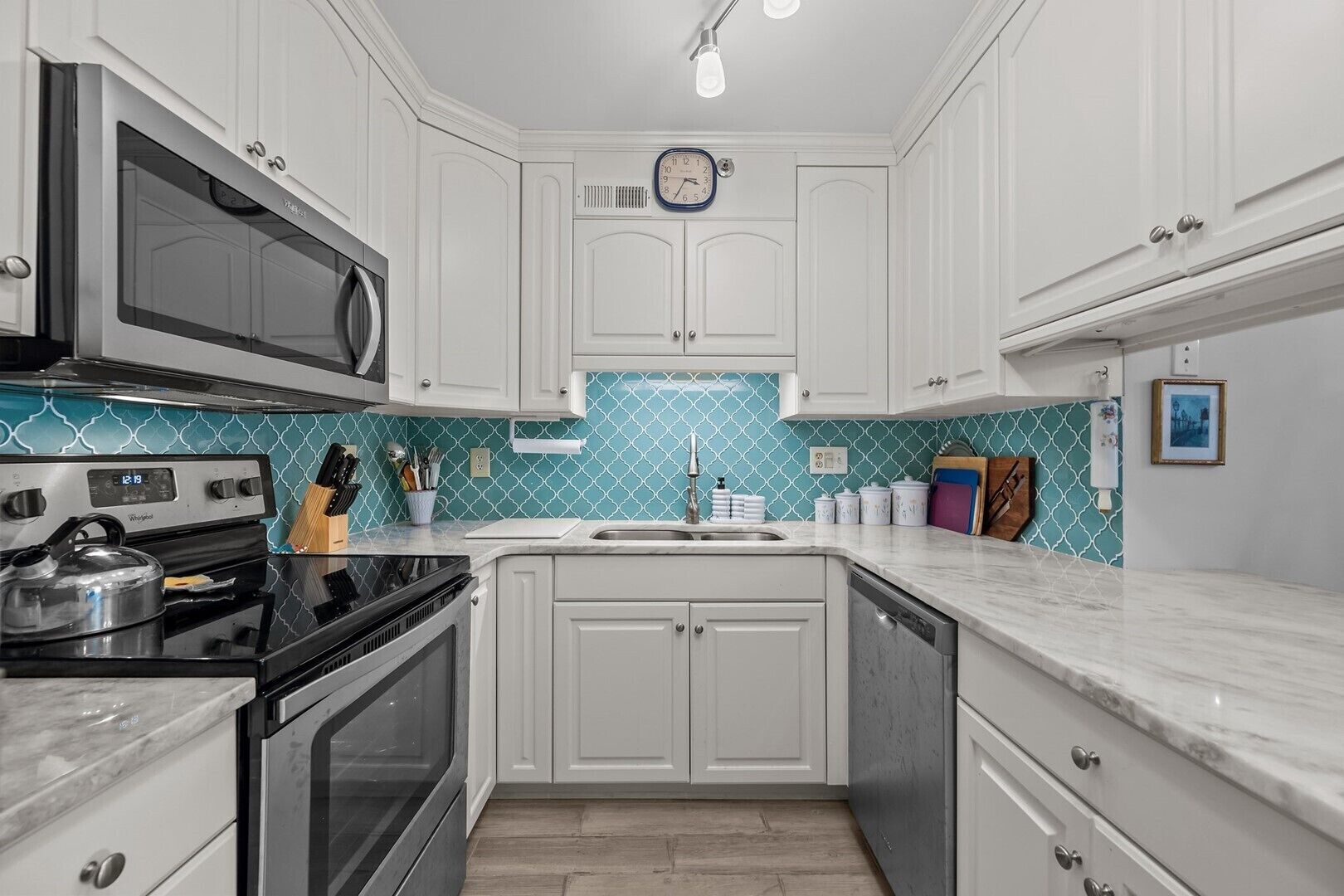 A compact kitchen with white cabinetry, a microwave, a stove, and a sink.