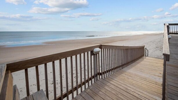 Une promenade en bois menant à une plage, avec un ciel dégagé.
