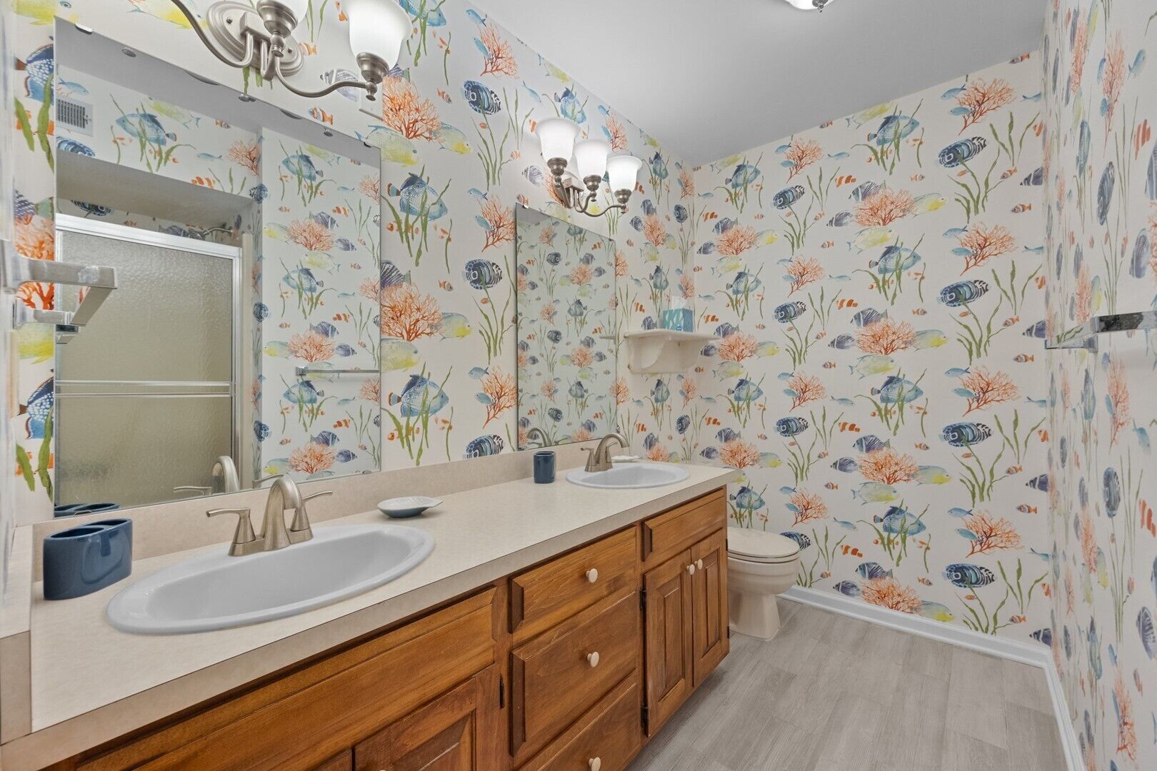 Une salle de bain avec deux lavabos, des meubles en bois, un grand miroir et un papier peint à motifs floraux.