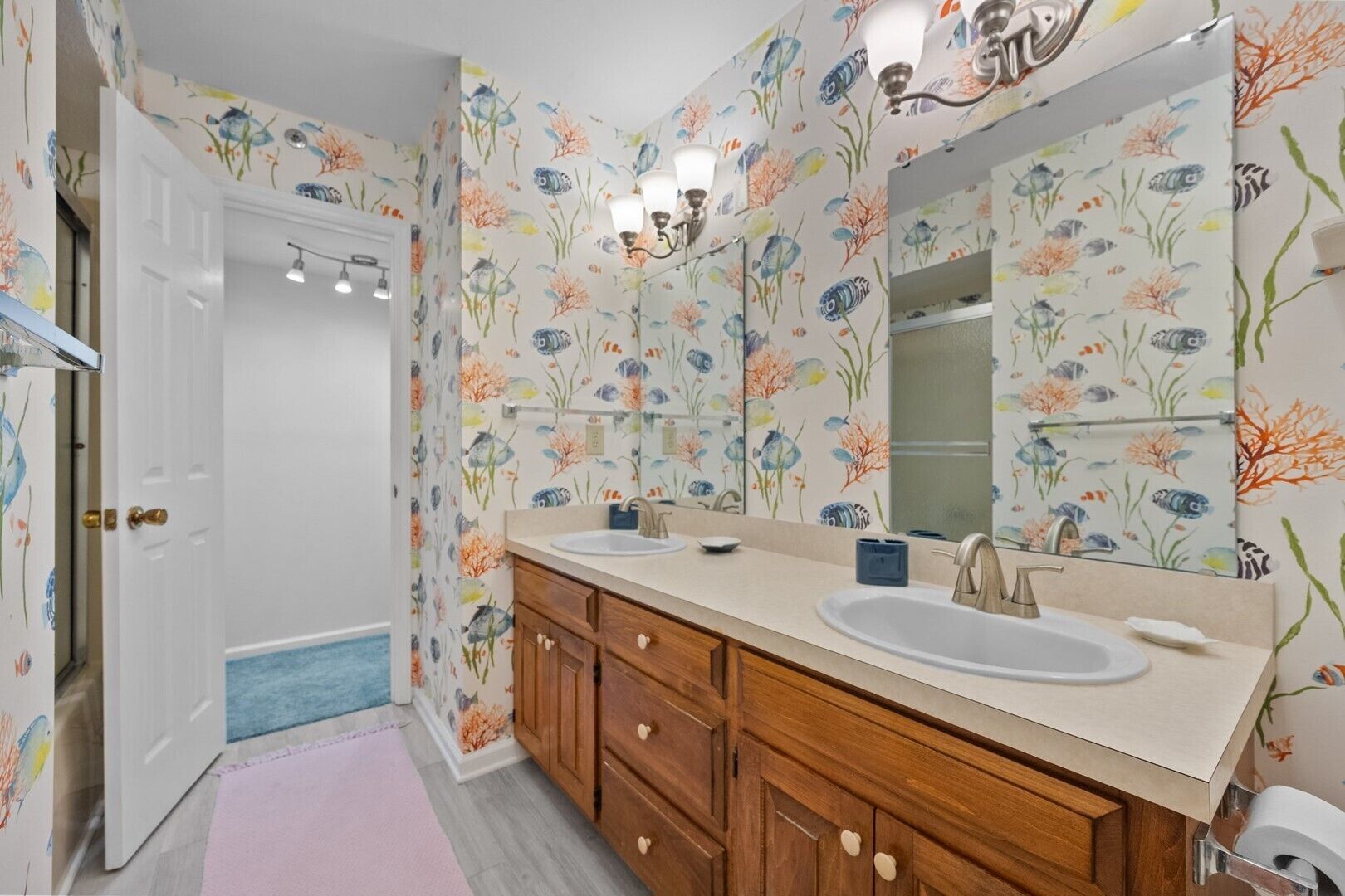 Un bagno con carta da parati a motivi floreali, un doppio lavabo, mobili contenitori in legno e un grande specchio.