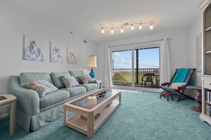 A living room with a sofa, coffee table, and a view of the outdoors. - Shipwatch 1105 - 2BR- 2BA - Oceanfront - Pool (North Topsail Beach)