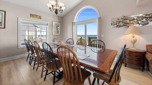 A dining area with a large table, chairs, a chandelier, and a view of the ocean through a large window. - 'A Sunny Delight - 6BR - Oceanfront - Sleeps 15 (North Topsail Beach)