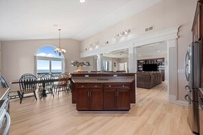 A spacious kitchen with a large island, wooden cabinets, and a dining area with chairs. - 'A Sunny Delight - 6BR - Oceanfront - Sleeps 15 (North Topsail Beach)