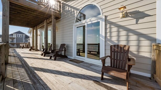 A wooden deck with chairs, a glass door, and a railing. - 'A Sunny Delight - 6BR - Oceanfront - Sleeps 15 (North Topsail Beach)