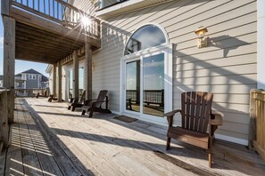 A wooden deck with chairs, a glass door, and a railing. - 'A Sunny Delight - 6BR - Oceanfront - Sleeps 15 (North Topsail Beach)