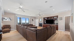 A spacious living area with a large sectional sofa, a fireplace, a television, and a bookshelf. - 'A Sunny Delight - 6BR - Oceanfront - Sleeps 15 (North Topsail Beach)