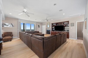 A spacious living area with a large sectional sofa, a fireplace, a television, and a bookshelf. - 'A Sunny Delight - 6BR - Oceanfront - Sleeps 15 (North Topsail Beach)