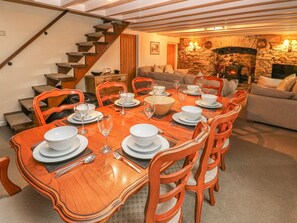 Comedor con mesa de madera dispuesta para seis personas, sillas anaranjadas, chimenea de piedra y una escalera.
