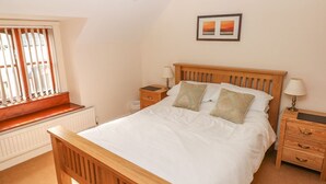 Une chambre à coucher avec un lit en bois, deux tables de chevet, une fenêtre avec des stores, un radiateur et un tableau encadré au mur.