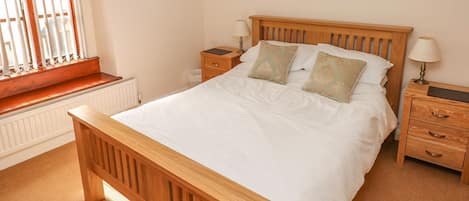 A bedroom with a wooden bed, two bedside tables, a window with blinds, a radiator, and a framed picture on the wall.