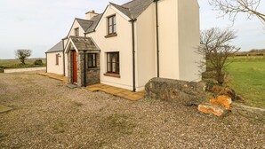Une maison à deux étages, avec des fondations en pierre, une porte rouge et une allée gravillonnée.