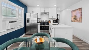 A modern kitchen with white cabinets, stainless steel appliances, and a glass dining table. - Modern Pad w/ Game Room Arcade! (San Diego)