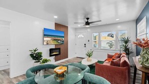A modern living room with a glass coffee table, a red sofa, and a TV mounted on the wall. - Modern Pad w/ Game Room Arcade! (San Diego)