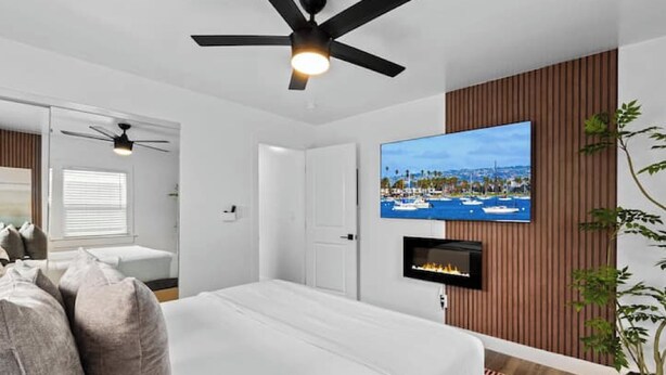 A bedroom with a bed, a ceiling fan, a TV mounted on the wall, and a fireplace. - Modern Pad w/ Game Room Arcade! (San Diego)