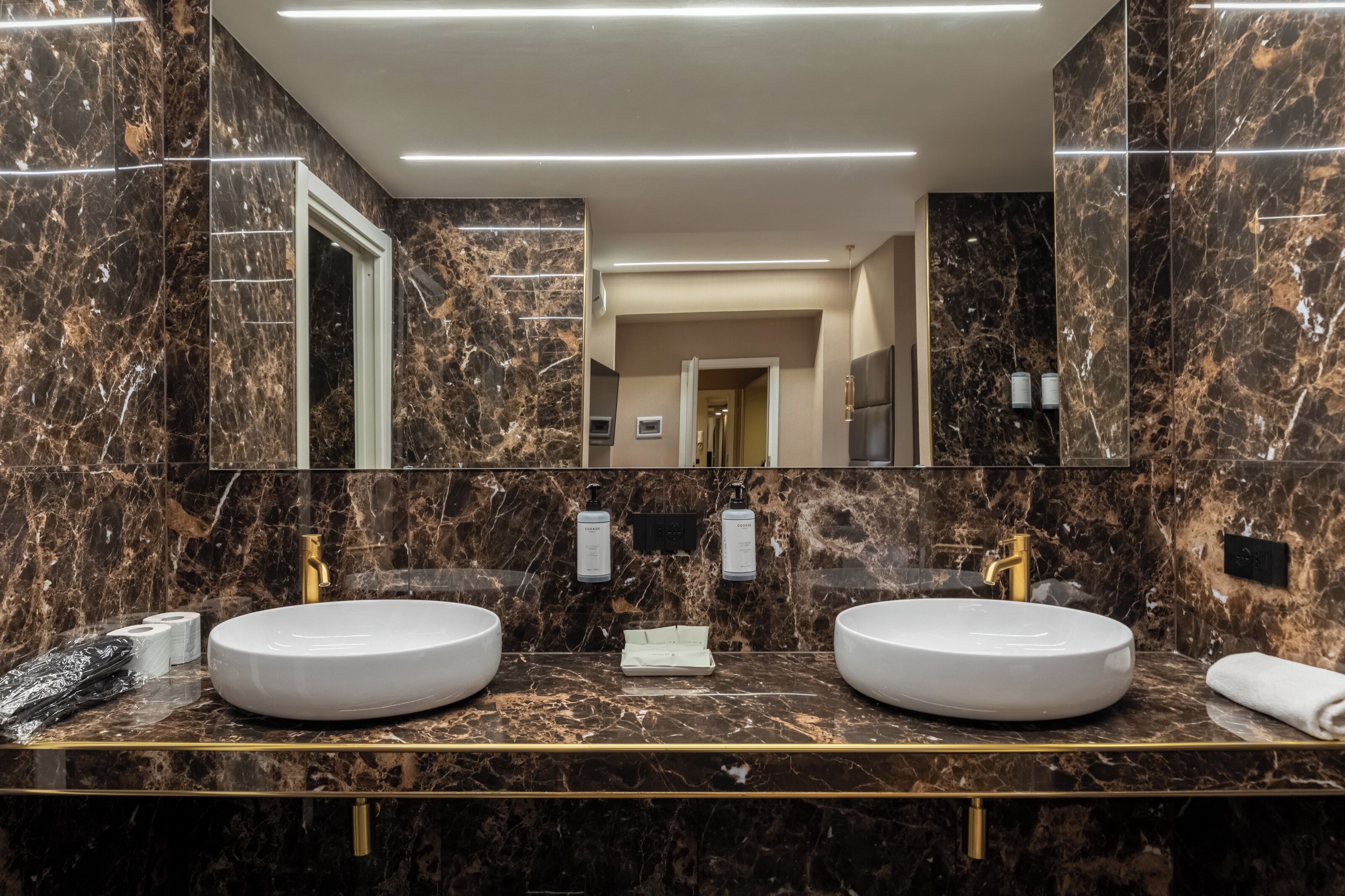 A modern bathroom with two sinks, marble walls, and a large mirror.