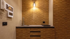 A kitchen with a wooden backsplash, a built-in sink, a light fixture above the counter, and a telephone mounted on the wall. - HELMIRAGE Frattina Suite (Rome)