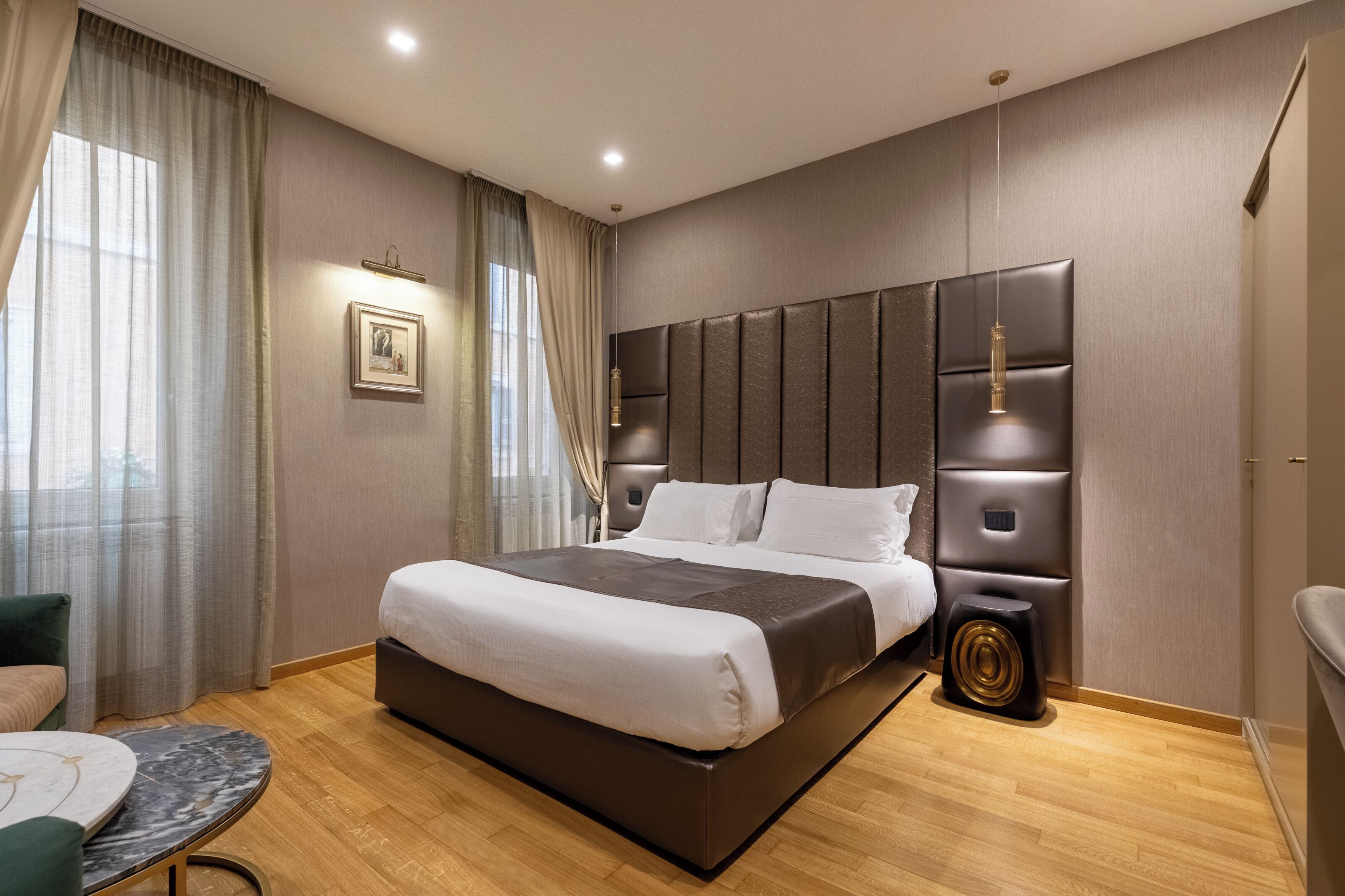 Une chambre d’hôtel moderne avec un grand lit, une table de chevet, une petite table ronde et une grande fenêtre avec des rideaux.