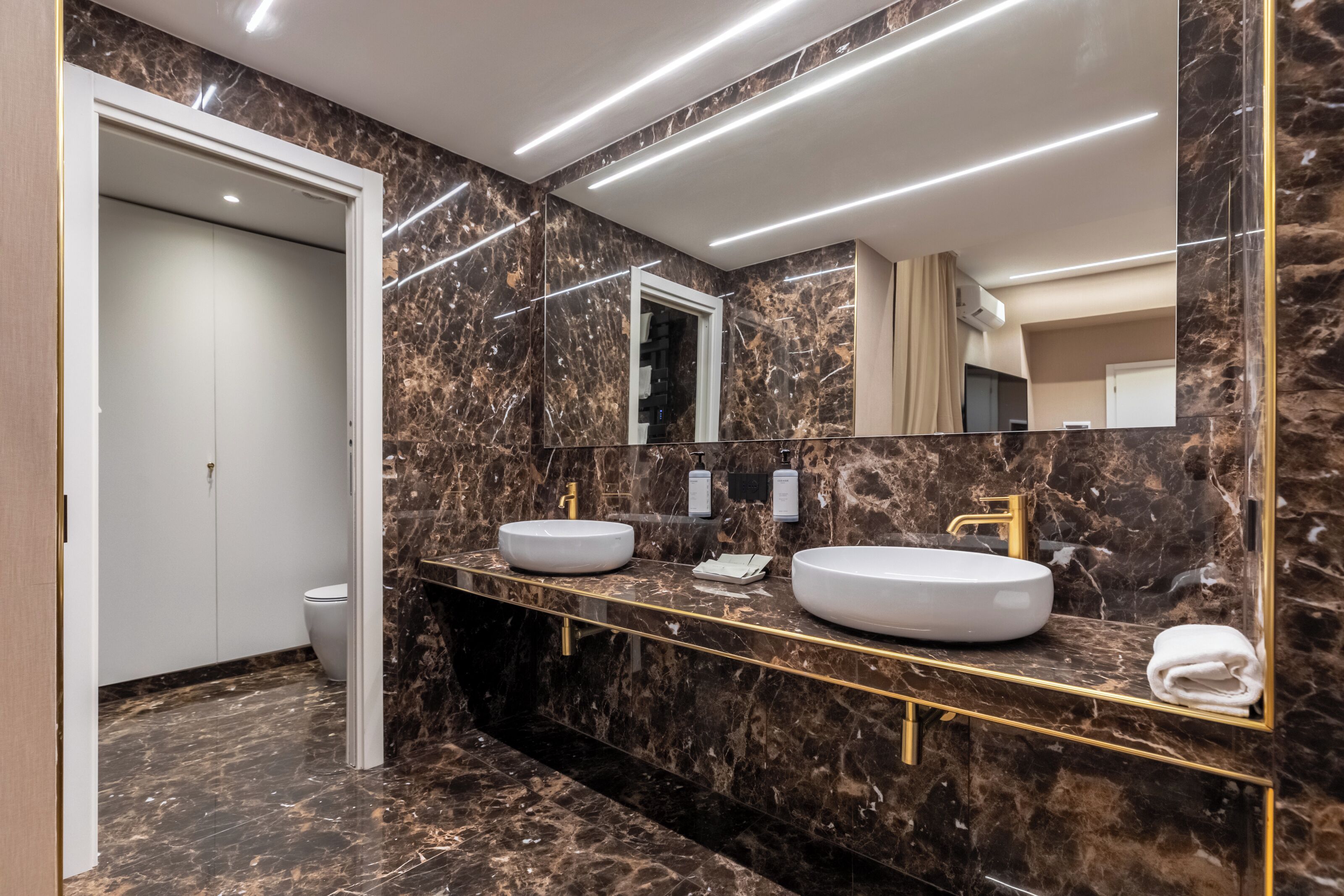 Une salle de bain moderne avec des murs en marbre, deux lavabos et un grand miroir.