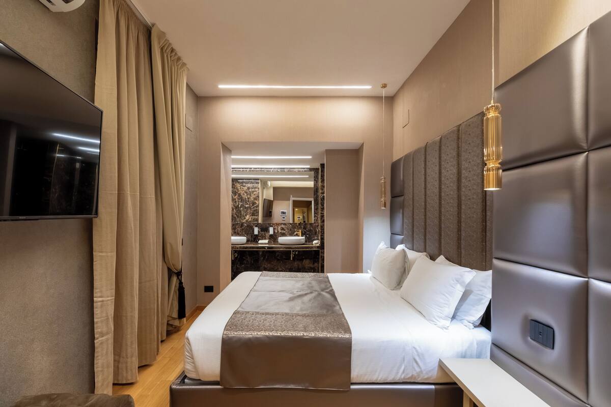 Une chambre d’hôtel moderne dotée d’un grand lit, d’une télévision, d’une coiffeuse avec des miroirs et d’un plafond bien éclairé.