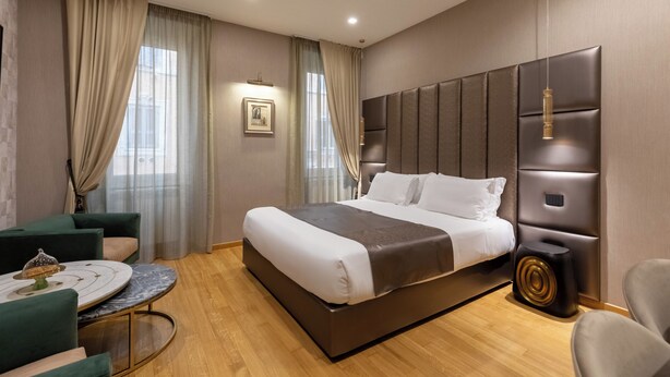 A modern hotel room with a large bed, a round table, and a seating area. - HELMIRAGE Frattina Suite (Rome)