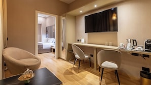 A modern hotel room with a dining area, a TV mounted on the wall, and a visible bed in the adjacent room. - HELMIRAGE Frattina Suite (Rome)