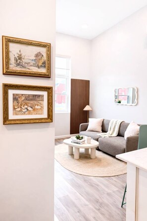 A modern living room with a grey sofa, a round coffee table, and two framed paintings on the wall. - Modern Loft Near Yale |Wooster Sq| 5 Star Location (New Haven)