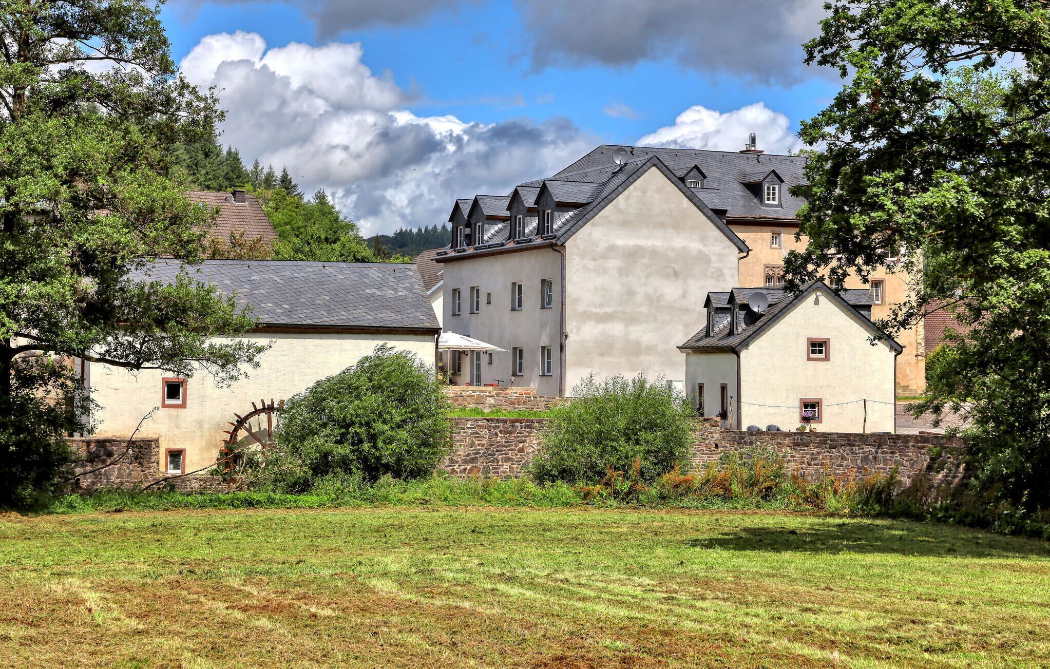 Ein traditionelles Steinhaus mit einem großen, zentralen Turm, umgeben von kleineren Gebäuden und üppigem Grün.