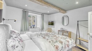 Un dormitorio con cama, una silla, televisor, espejo y ventana con cortinas.