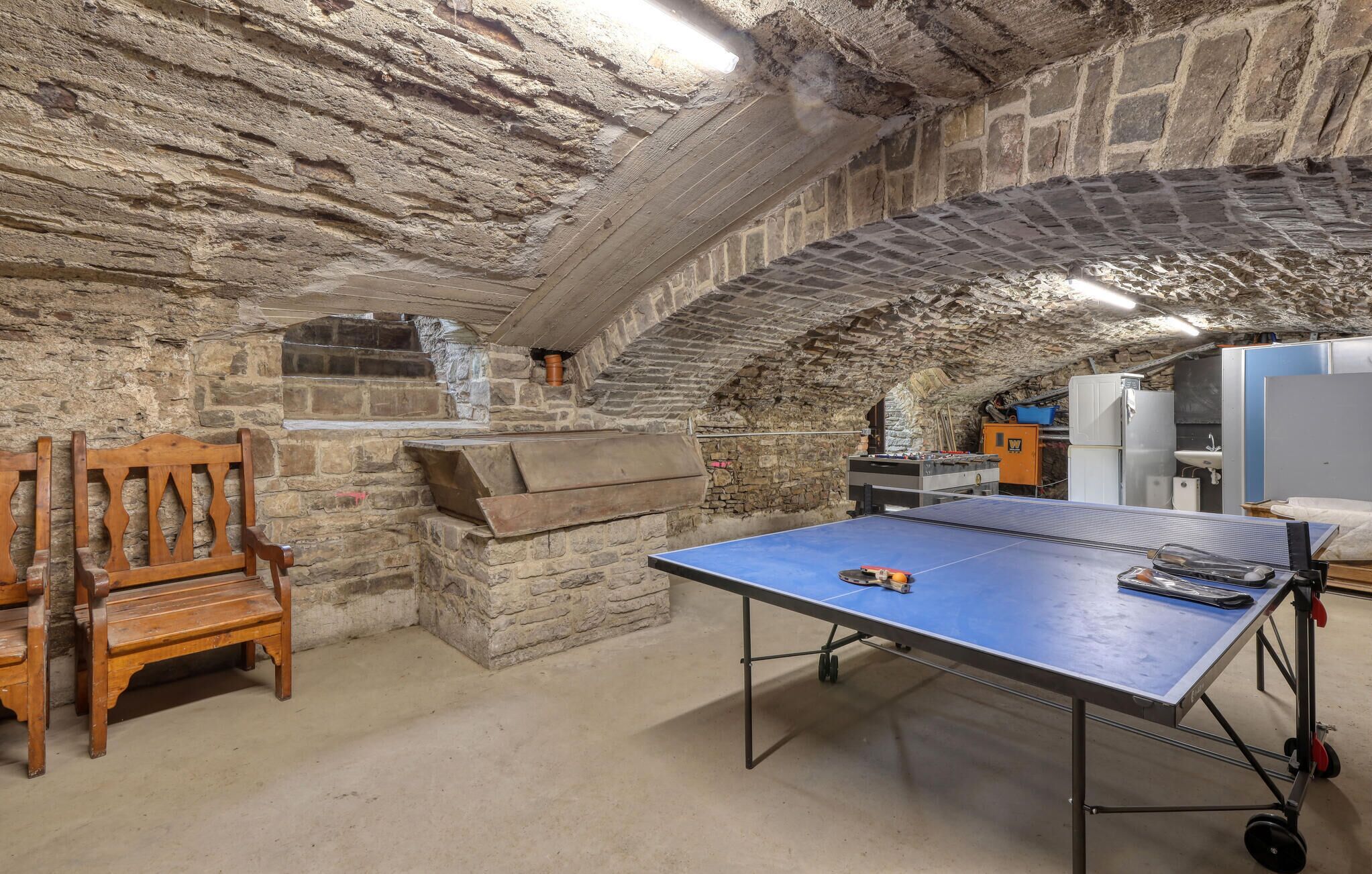 A stone-walled room with a ping pong table, a wooden chair, and a small kitchenette.