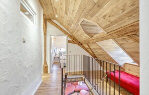Eine Holztreppe führt zu einem Schlafzimmer auf dem Dachboden, mit einem roten Bett und einem Dachfenster.