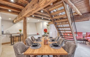 Ein Essbereich mit einem Holztisch, gedeckt für sechs Personen, umgeben von grauen, gepolsterten Stühlen. Eine Holztreppe mit Metallgeländer ist rechts zu sehen.