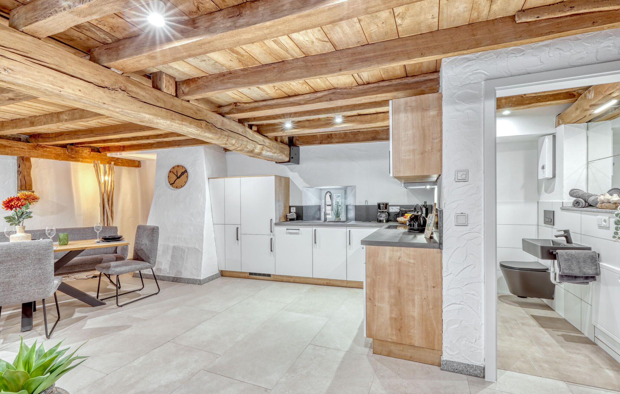 Une cuisine moderne avec des armoires blanches, un plafond en bois et un coin repas comprenant une table et des chaises.