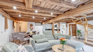 Amplia sala de estar con techo de madera, un conjunto de sofás, una mesa de comedor y una cocina al fondo.