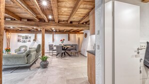Un interior moderno con vigas de madera a la vista, un comedor con mesa y sillas, y una cocina con armarios blancos.