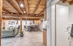 Un interior moderno con vigas de madera a la vista, un comedor con mesa y sillas, y una cocina con armarios blancos.