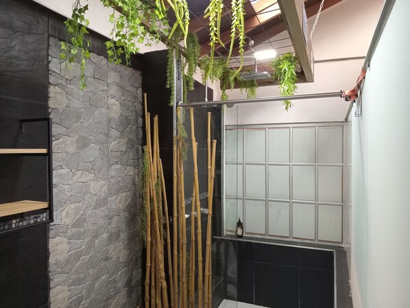 Casa de banho com parede de pedra, plantas de bambu e cabine de chuveiro em vidro.