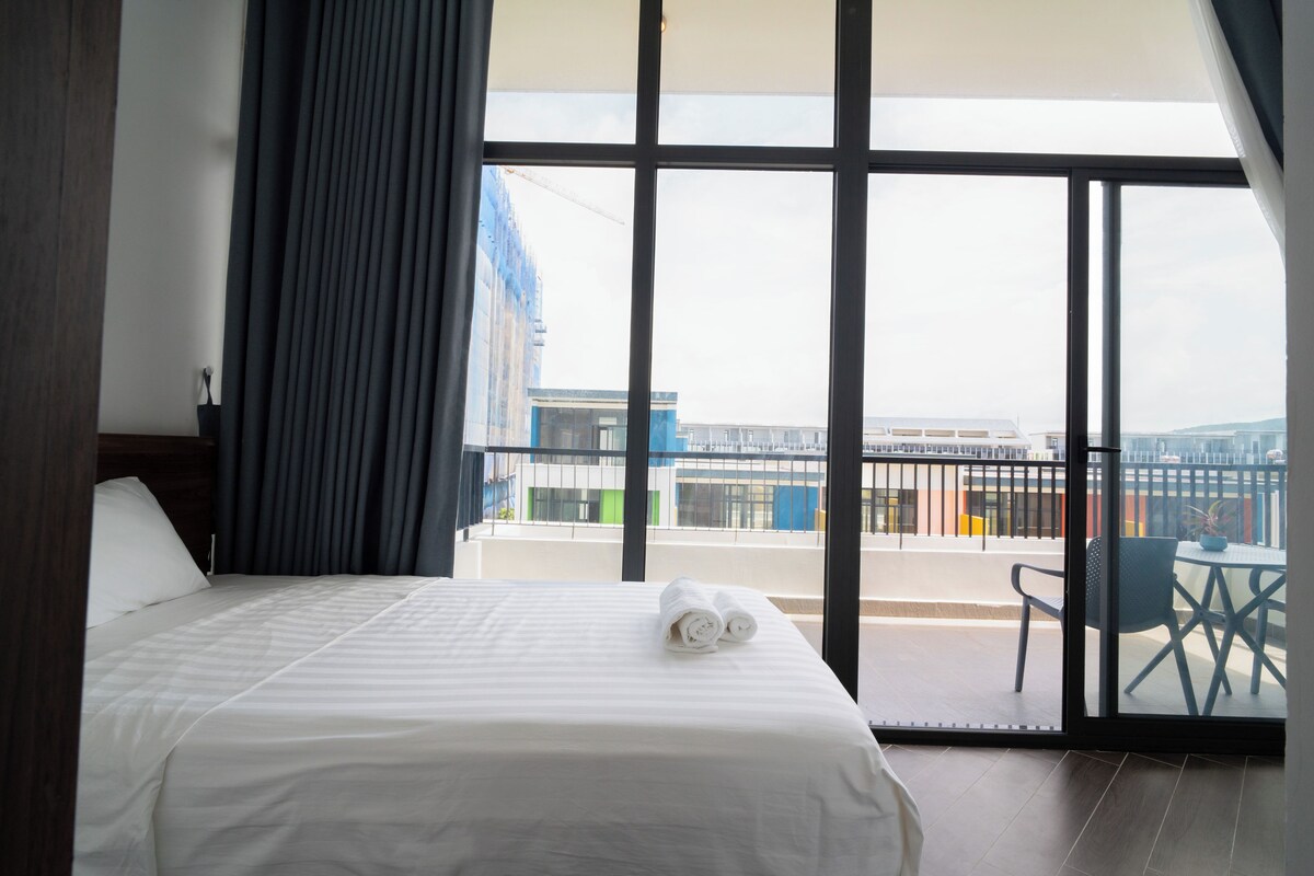 A hotel room with a large window, a bed, a chair, and a view of the cityscape.