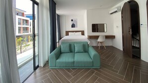 Et hotelværelse med en seng, en grøn sofa, et skrivebord, et spejl og udsigt til bygninger.